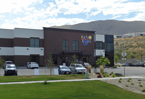 Exterior of a building labeled "Kid Logic," surrounded by parking and mountains in the background under a cloudy sky.