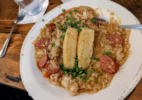 A plate of jambalaya with chicken, sausage, and green onions, served with two pieces of cornbread on top.