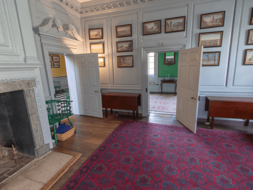 A spacious room with wooden floors, framed pictures on the walls, and open doors leading to another area.
