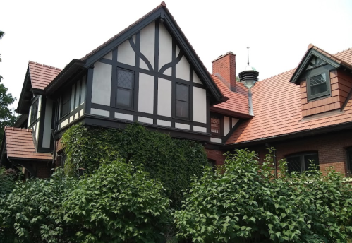 A charming Tudor-style house with ivy-covered walls and a red-tiled roof, surrounded by lush greenery.
