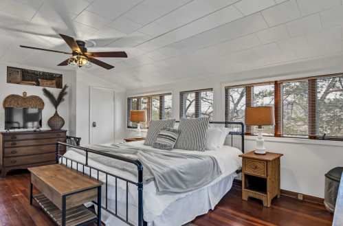 Cozy bedroom with a metal bed frame, wooden furniture, and large windows letting in natural light.