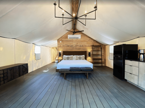 Spacious glamping tent interior with a bed, wooden accents, and modern amenities like a fridge and coffee maker.
