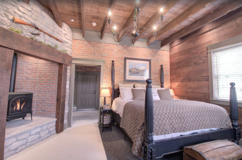 Cozy bedroom with a wooden bed, brick walls, and a fireplace, featuring rustic decor and warm lighting.