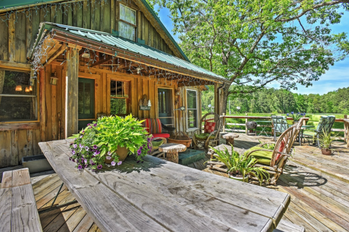 A rustic wooden cabin with a spacious deck, surrounded by greenery and decorated with potted plants and outdoor seating.