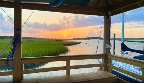 A serene sunset view over a marsh, framed by wooden beams and a boat docked nearby.