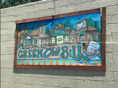 Colorful mural featuring "Green Chili Bill" with a whimsical town scene and a smiling character in a hat.
