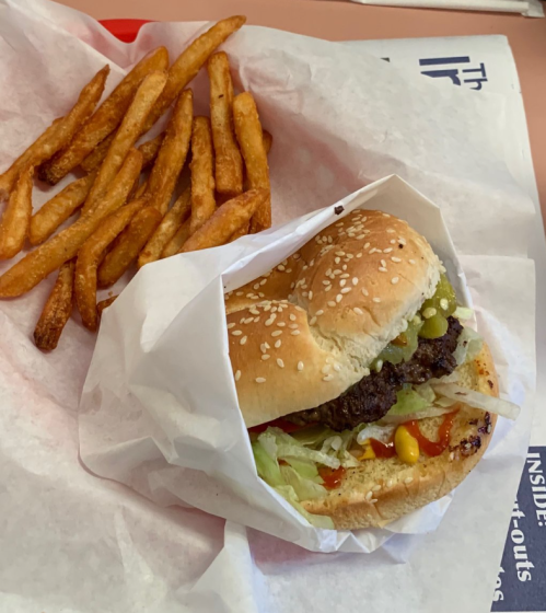 A sesame seed bun burger with lettuce, pickles, and mustard, served with a side of crispy French fries.