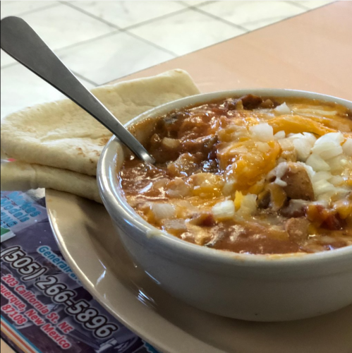 A bowl of chili topped with cheese and onions, served with two pieces of flatbread on the side.