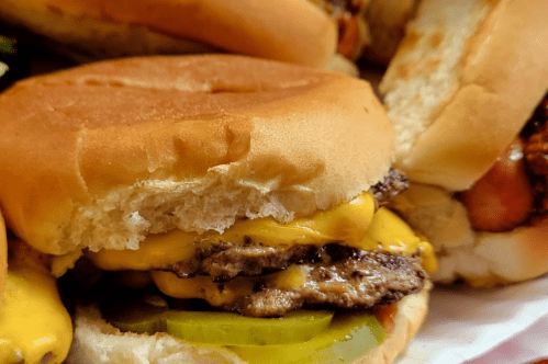 Close-up of a cheeseburger with two layers of melted cheese, pickles, and a soft bun.