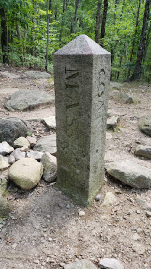 Stone boundary marker between Massachusetts and Connecticut, surrounded by rocks in a wooded area.