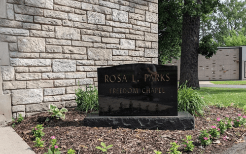 Black granite memorial stone for Rosa L. Parks, inscribed with "Freedom Chapel," surrounded by greenery.