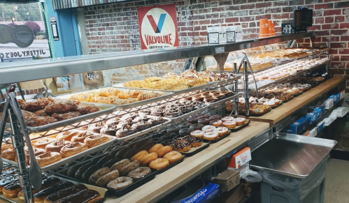 A display case filled with a variety of donuts, including glazed, chocolate, and sprinkled options, in a cozy shop.