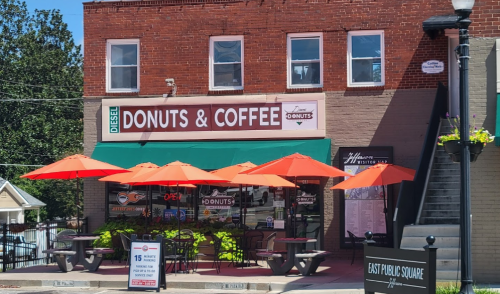 A cozy donut and coffee shop with orange umbrellas outside, located in a brick building near a public square.