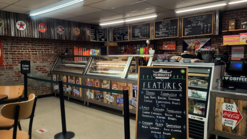 A cozy café interior with a display case of pastries, a menu board, and seating. Brick walls and a welcoming atmosphere.