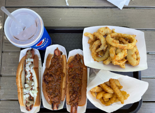 A tray with two chili dogs, a side of onion rings, crinkle fries, and a soda.