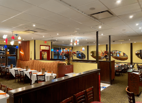 Interior of a restaurant featuring tables with white tablecloths, colorful hanging lights, and decorative mirrors.