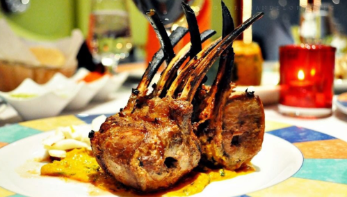 Grilled lamb chops with charred bones, served on a colorful plate with a sauce and garnishes.