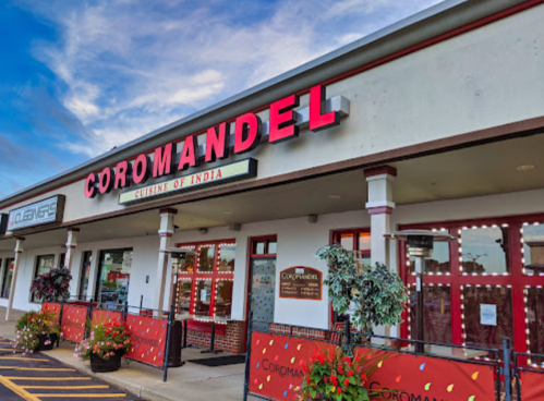 Exterior of Coromandel, a restaurant featuring Indian cuisine, with colorful signage and decorative plants.