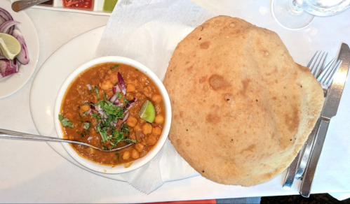 A bowl of chickpea curry garnished with cilantro and lime, served with a large, round flatbread on a white plate.