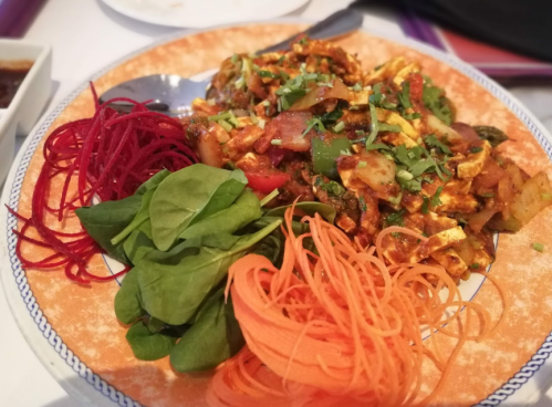 A colorful plate featuring sautéed vegetables, paneer, and garnishes of beetroot, spinach, and carrot.