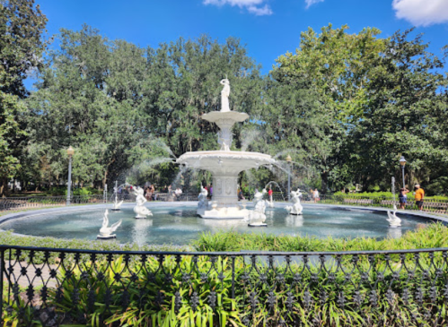 A large white fountain with statues in a park, surrounded by greenery and people enjoying the scenery.