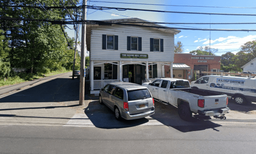 A two-story building with a sign reading "The Rock Hill Store," surrounded by parked vehicles and trees.