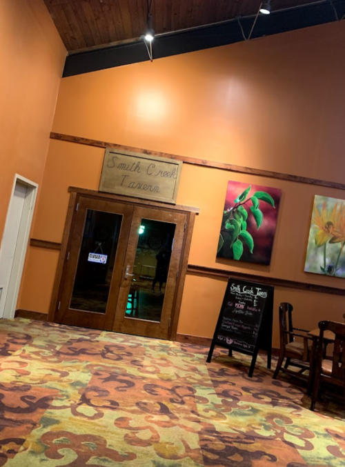 Interior of a restaurant with orange walls, wooden doors labeled "Smith Creek Tavern," and colorful artwork.