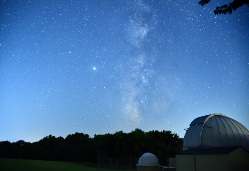 A clear night sky filled with stars and the Milky Way, with an observatory dome in the foreground.
