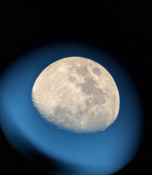 A close-up view of the moon, showcasing its craters, against a dark blue background.