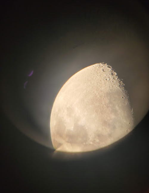 Close-up view of the moon's surface, showing craters and texture through a telescope lens.