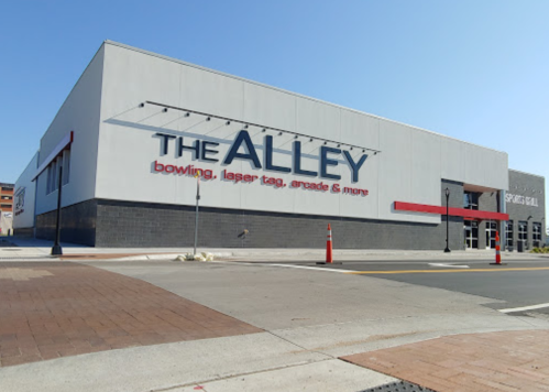 Exterior of The Alley building featuring bowling, laser tag, and arcade games, with clear blue sky above.