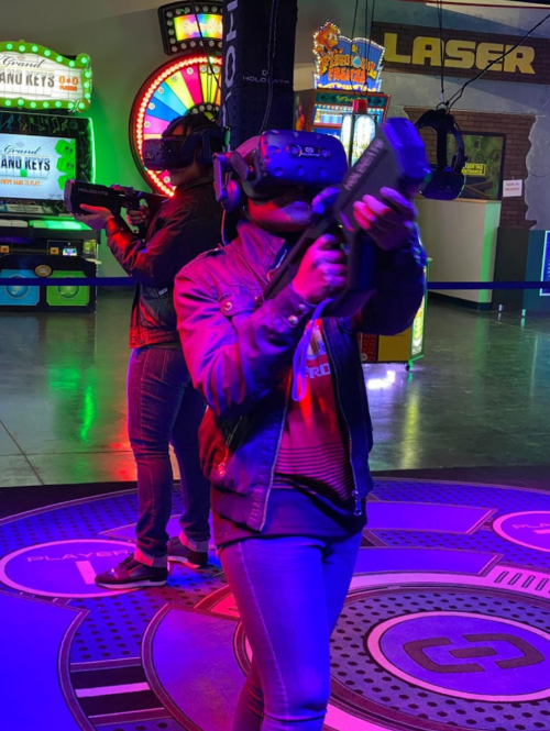 Two people in VR headsets holding guns in a colorful arcade setting with neon lights.