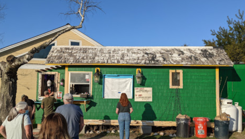 A colorful green building with a menu board, people waiting outside, and a tree branch extending over the roof.