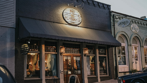 A cozy storefront with a sign reading "The Vintage Shop," featuring large windows and an awning, set in a charming street.