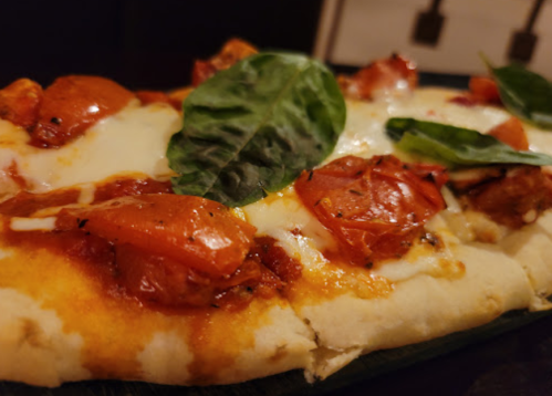 Close-up of a pizza topped with melted cheese, roasted tomatoes, and fresh basil leaves on a wooden board.