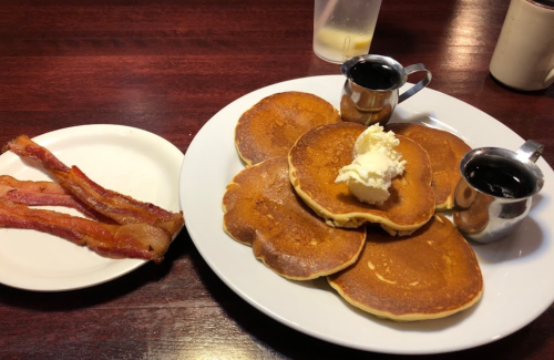 A plate of fluffy pancakes topped with butter and syrup, alongside a side of crispy bacon strips.
