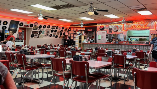 A retro diner with red booths, checkered floors, and vintage decor, featuring a lively atmosphere and music-themed walls.