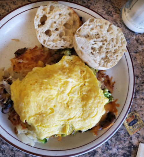 A plate with a fluffy omelet, hash browns, and two halves of an English muffin.