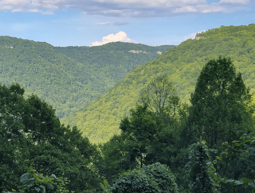 Lush green mountains under a blue sky with scattered clouds, showcasing a serene natural landscape.