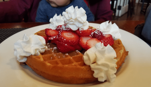A golden waffle topped with whipped cream and fresh strawberries, served on a white plate.