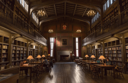 A spacious library with wooden shelves, chandeliers, and people reading at tables under warm lighting.