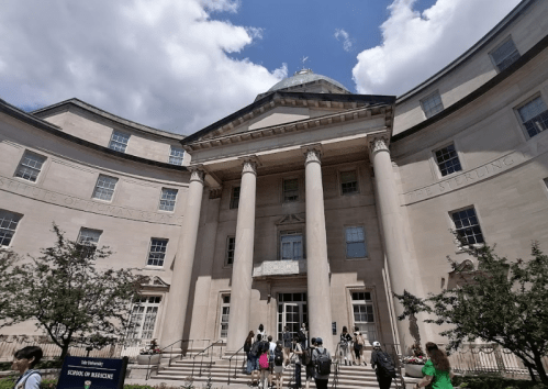 A large, classical building with a dome and columns, featuring people walking in front on a sunny day.