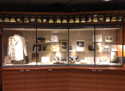 Display case featuring historical artifacts, photographs, and documents, including a white coat and books.