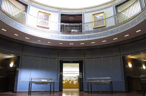 Interior view of a circular room with blue walls, framed portraits, and a staircase leading to an upper level.