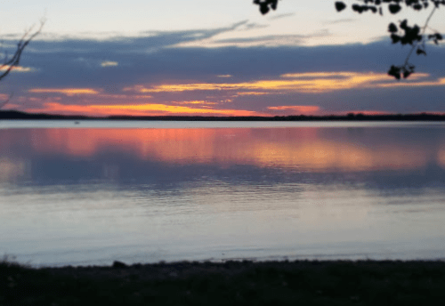 A serene lake at sunset, reflecting vibrant colors in the water with a cloudy sky above.
