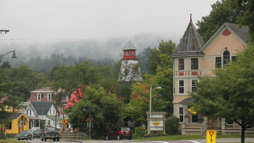 A quaint town scene with colorful houses, a lighthouse tower, and foggy mountains in the background.