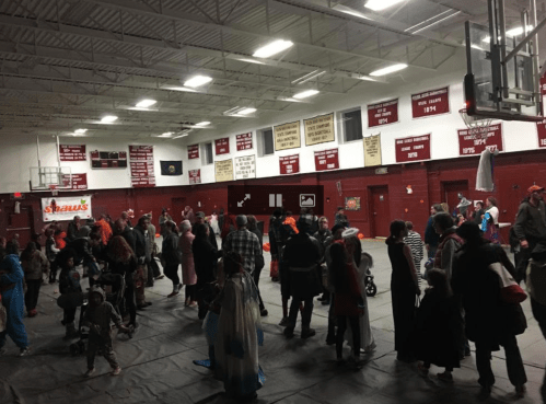 A gymnasium filled with people in costumes, celebrating a festive event with decorations and banners on the walls.