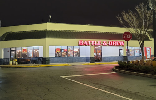 A brightly lit restaurant exterior at night, featuring the sign "BATTLE & BREW" and a stop sign nearby.