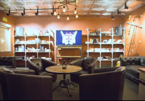 Cozy lounge with leather chairs, a round table, and shelves filled with books and decor, featuring a TV on the wall.