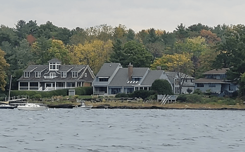 A scenic view of waterfront homes surrounded by trees with autumn foliage, seen from the water.